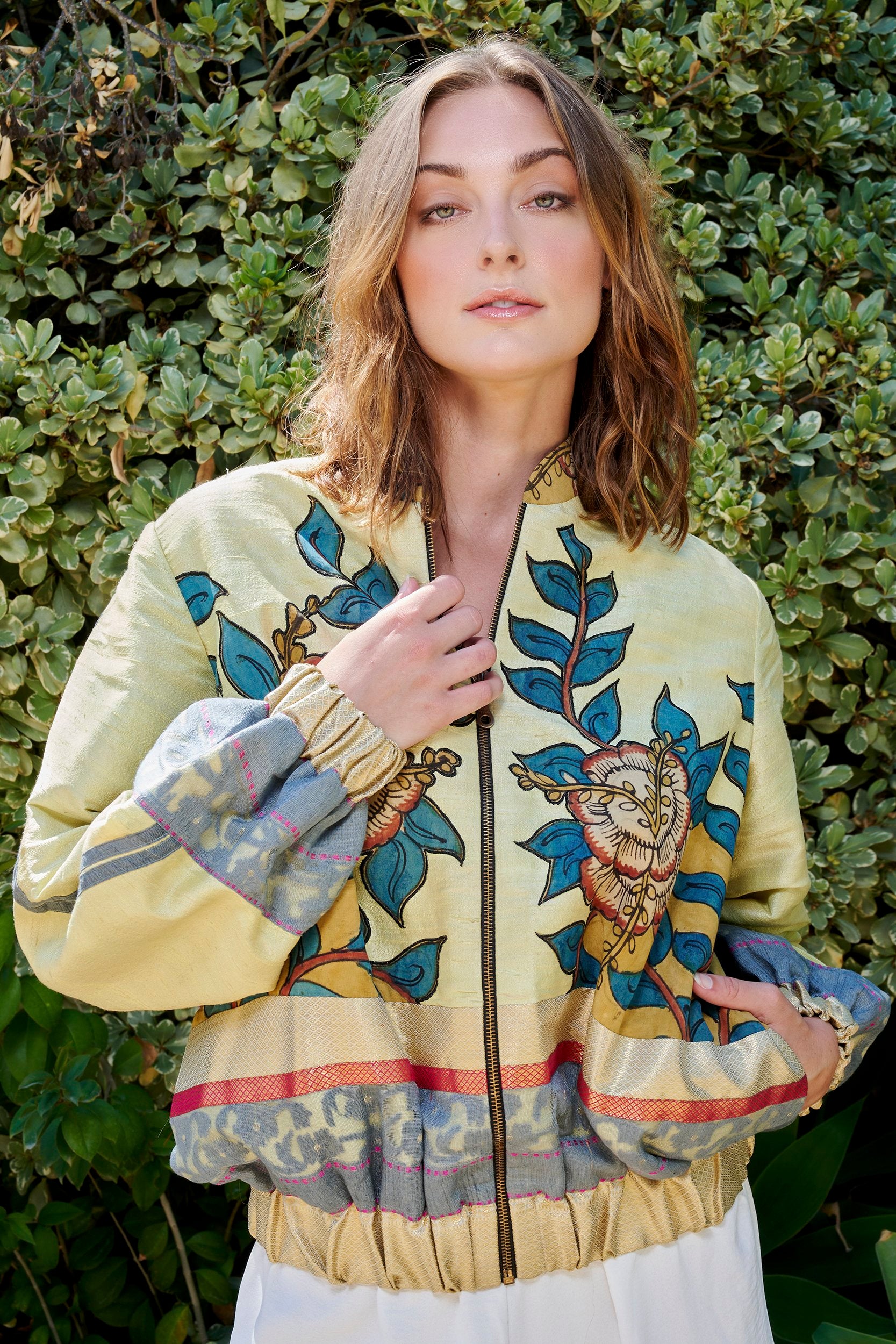A woman wearing a yellow with teal floral print bomber jacket . Handmade from repurposed precious fabric remnants.