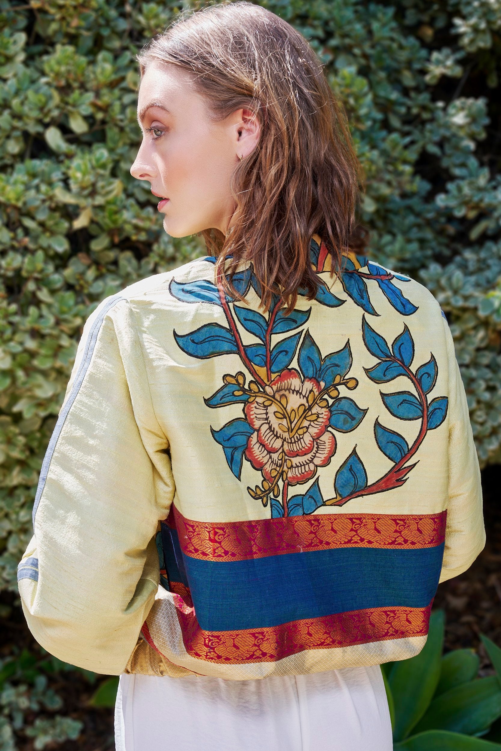 A woman wearing a handmade bomber jacket  with a large teal blue floral print on the back of the jacket. 
