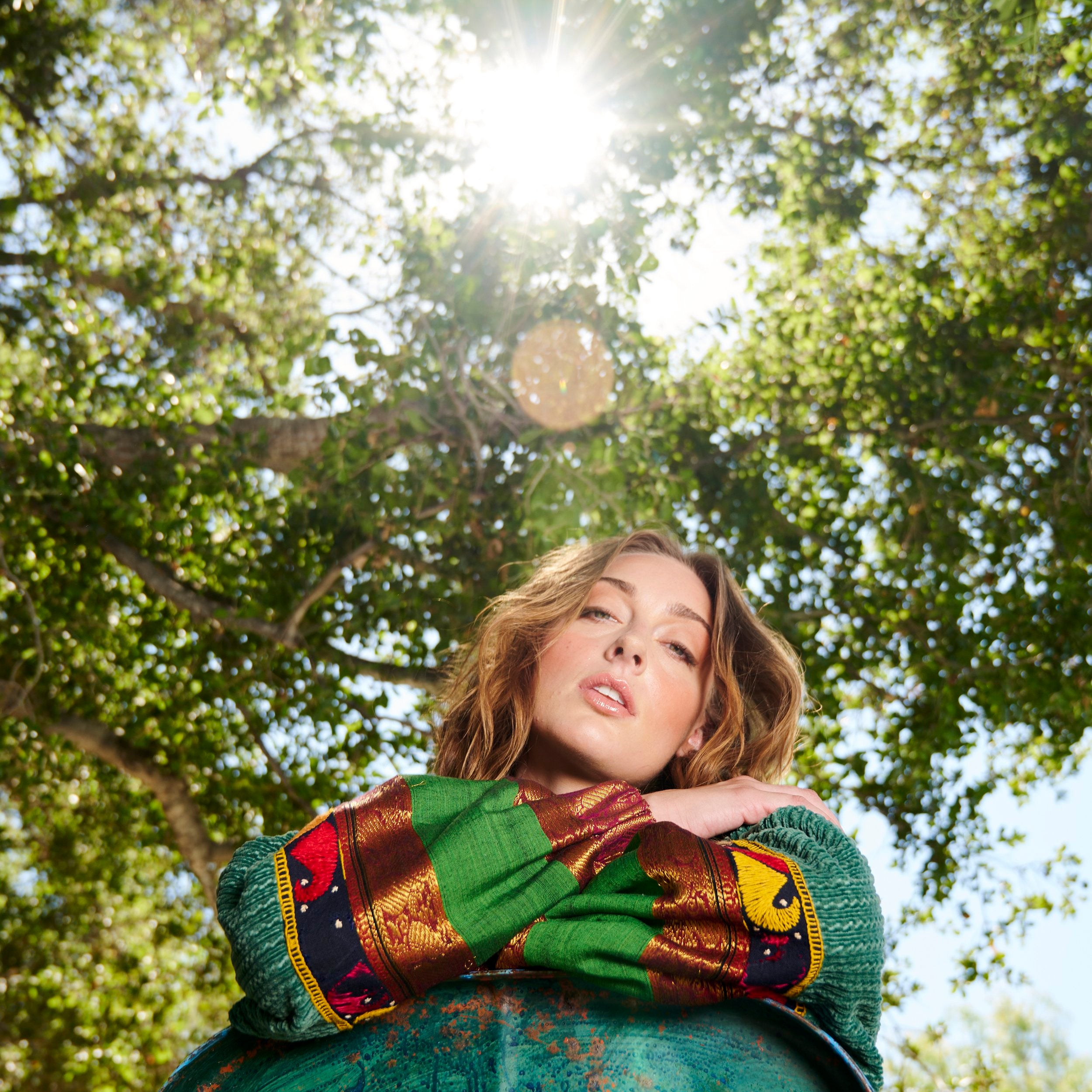 Model resting her folded arms on the chair wearing a green patchwork bomber jacket.