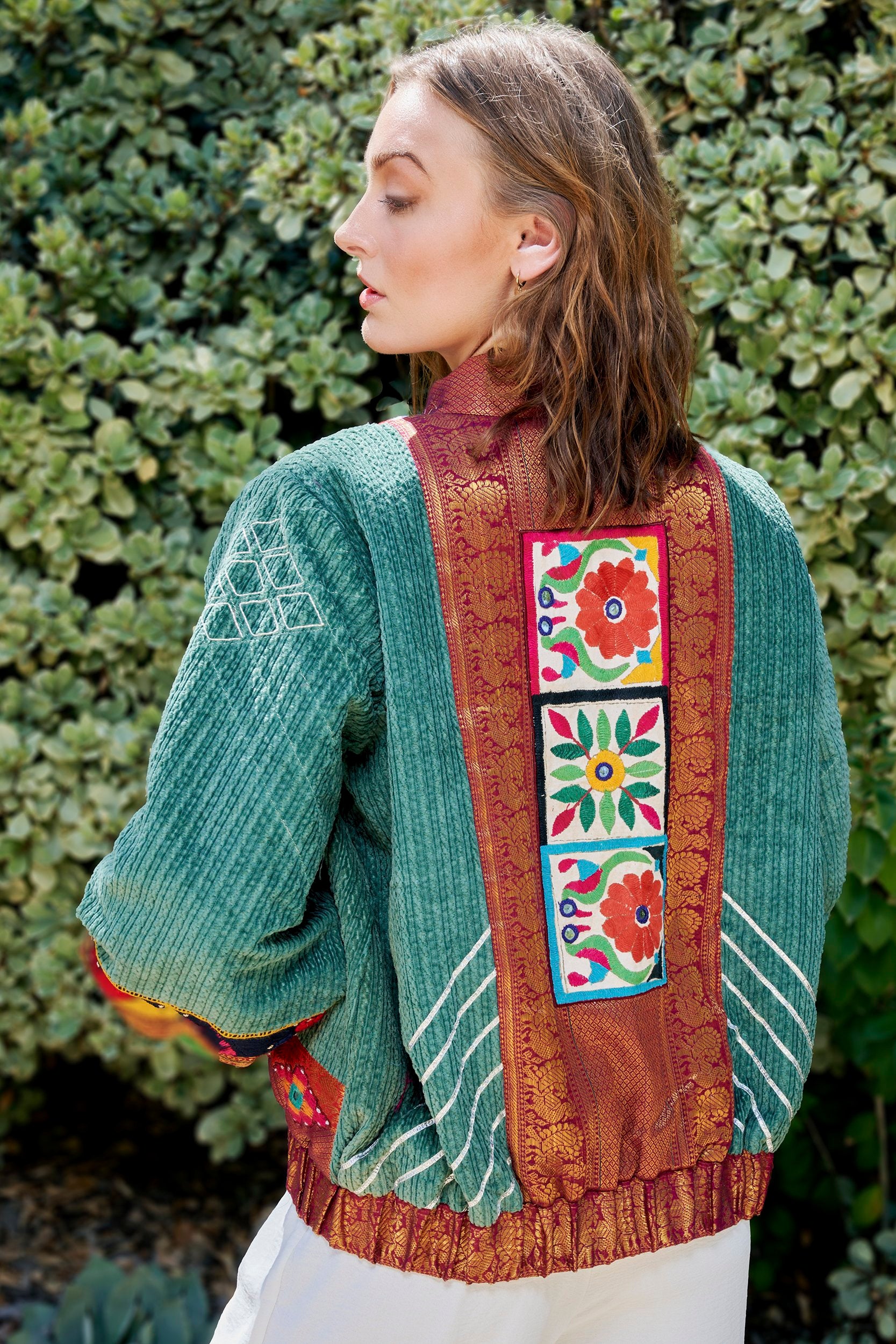Model showcasing artisanal craftsmanship of a bomber jacket with embroidered patch on the back of a jacket.