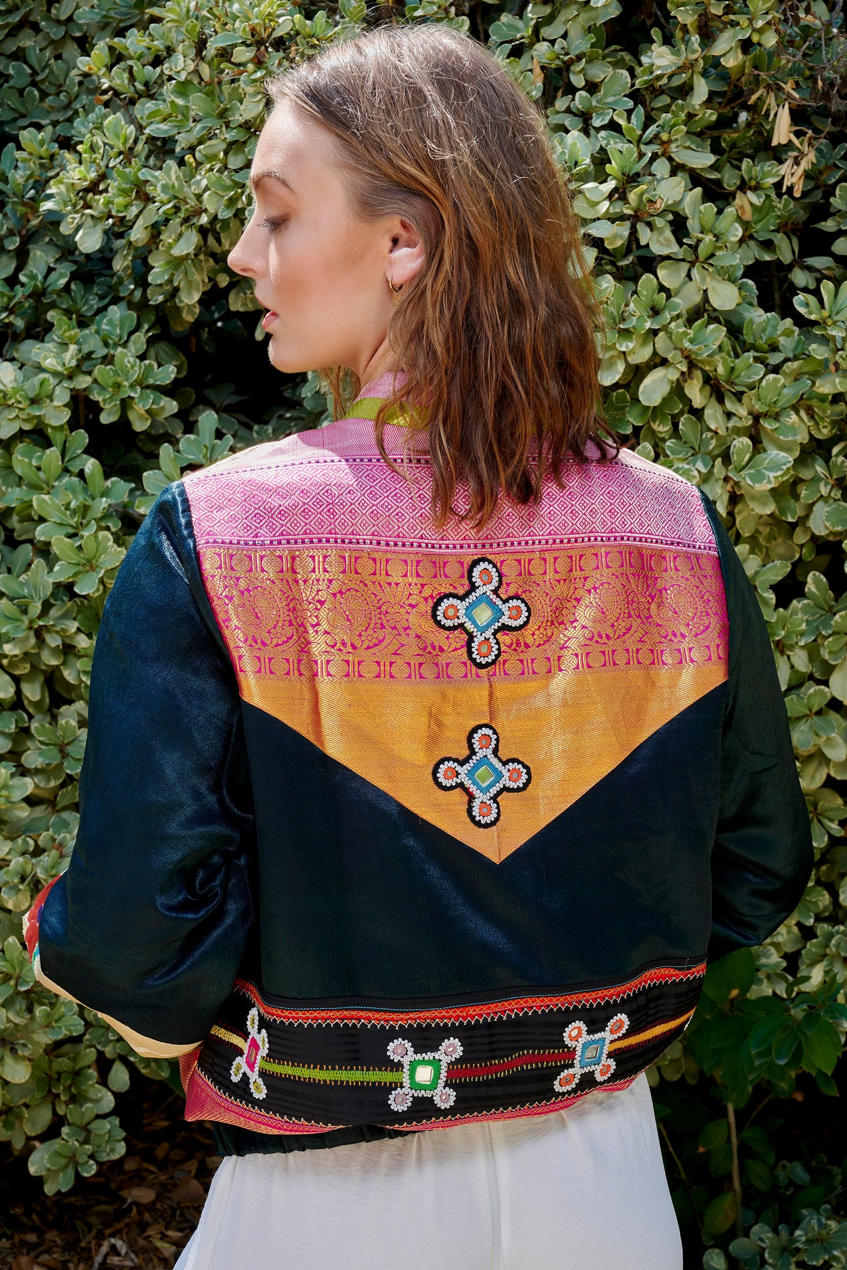 A woman wearing a designer Bomber Jacket with embroidery on the back of the jacket with patches. 