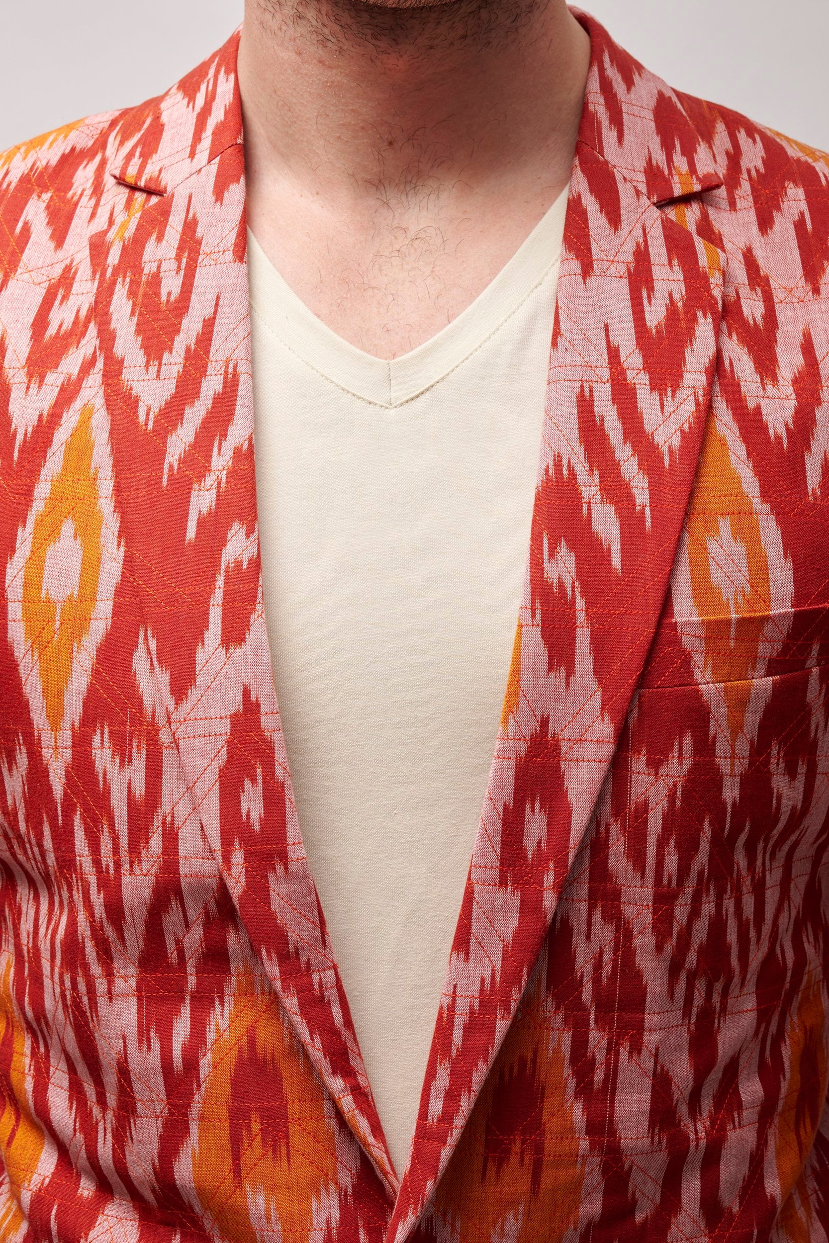 Closeup shot of Model wearing a coral blazer with bright contrast hues and showing the crisscross stitch lines.