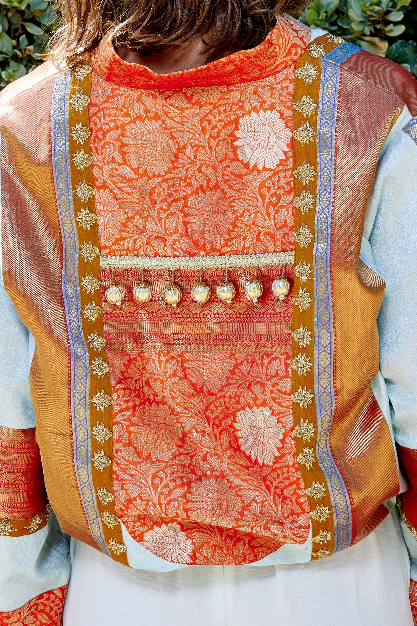 closeup of a bomber jacket showing details of gold embellishments and intricate zari weave pattern.