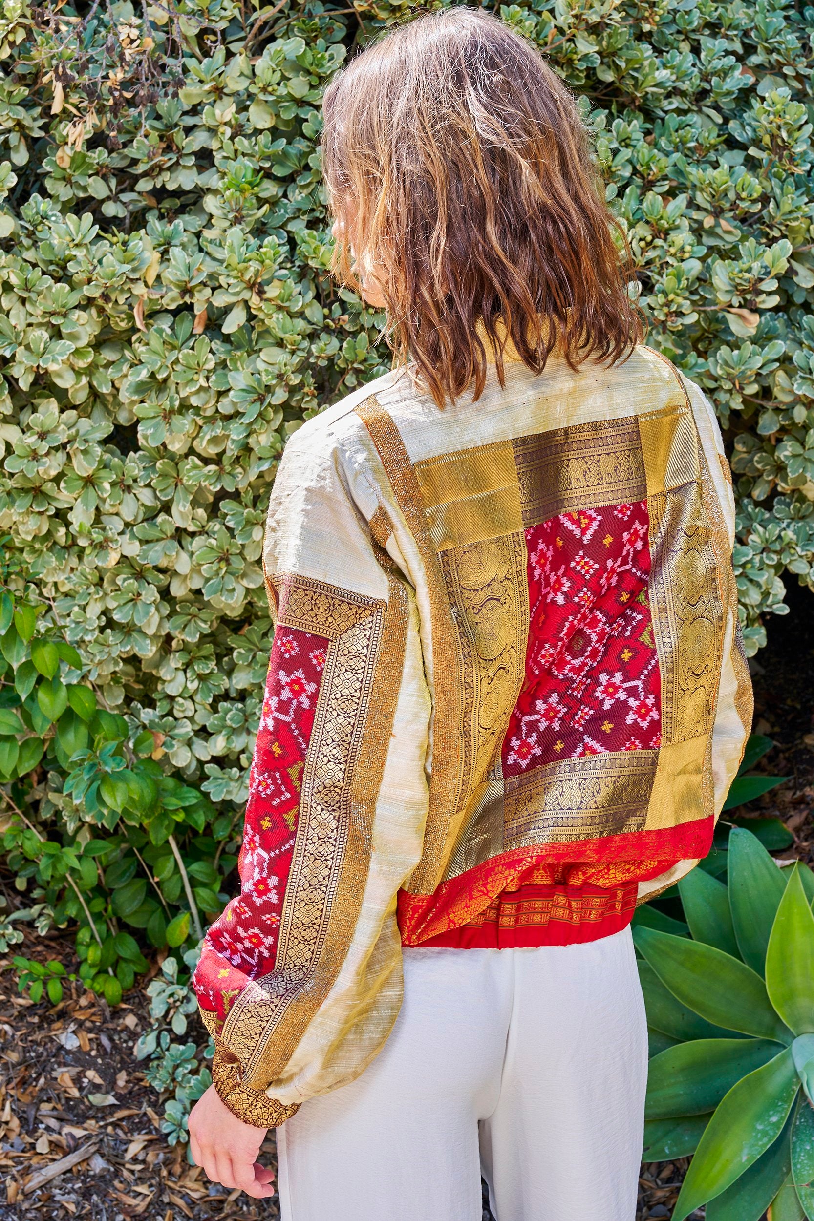 Model wearing a women's bomber jacket with patches on the back and sleeves.. Made from repurposed fabric.