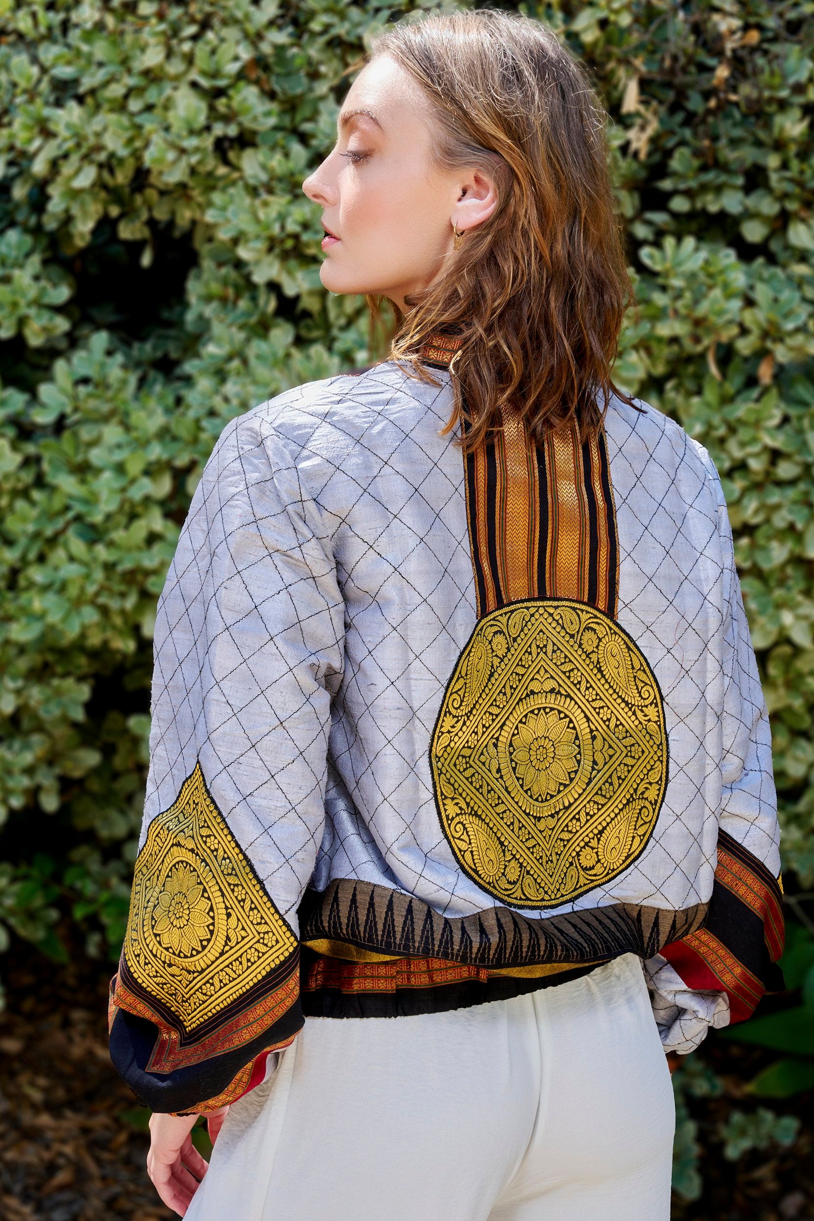 Women wearing a gray bomber jacket with a large gold embroidered patch on the back and sleeve.