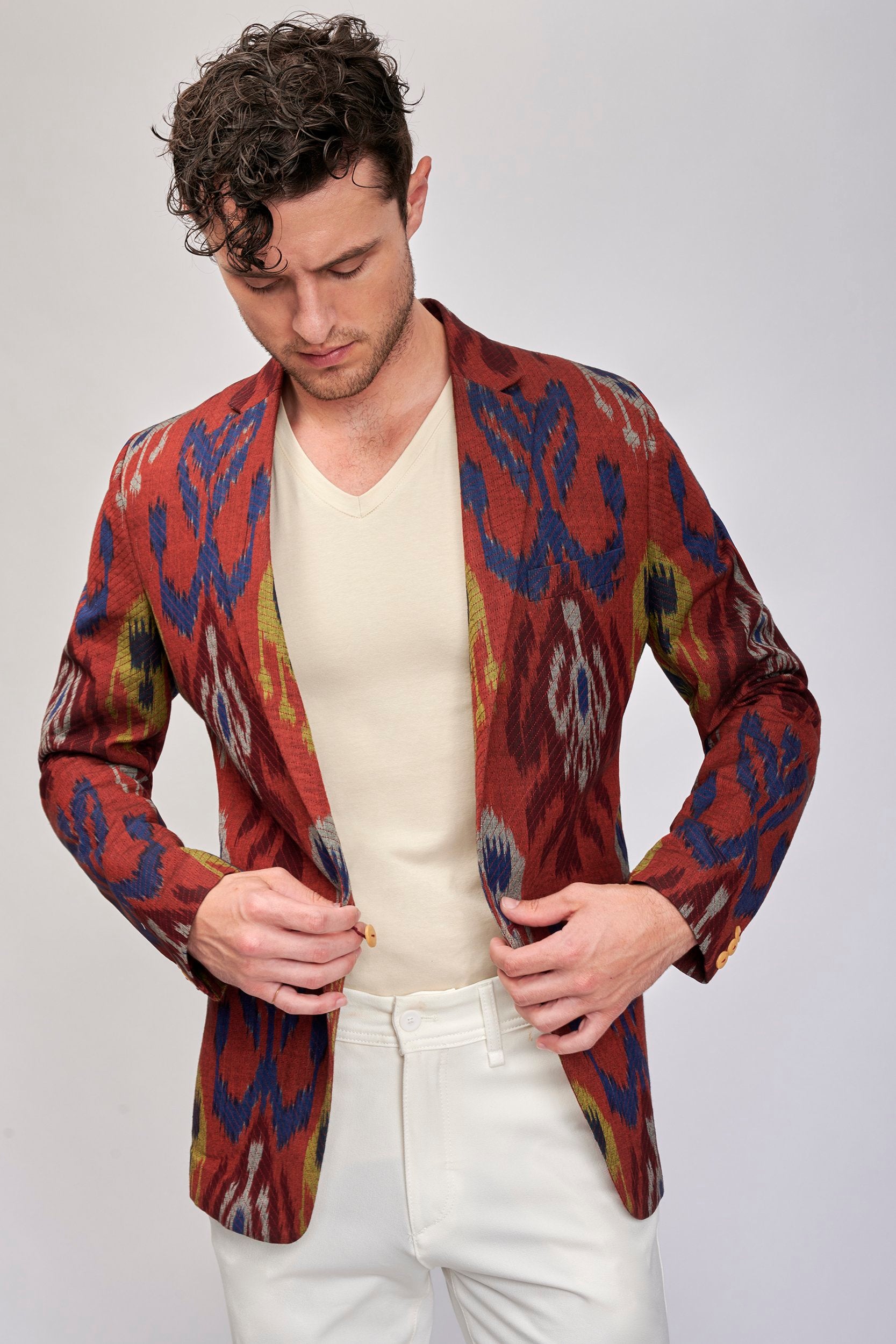 Model wearing a brick-red jacket with a bold pattern. It is hand-woven in the ancient art of Ikat.