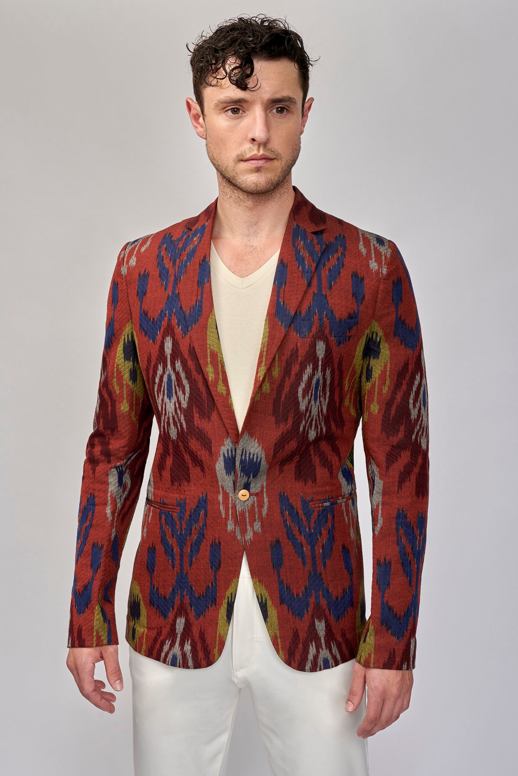 Model wearing a brick-red blazer with a bold pattern. It is hand-woven in the ancient art of Ikat.