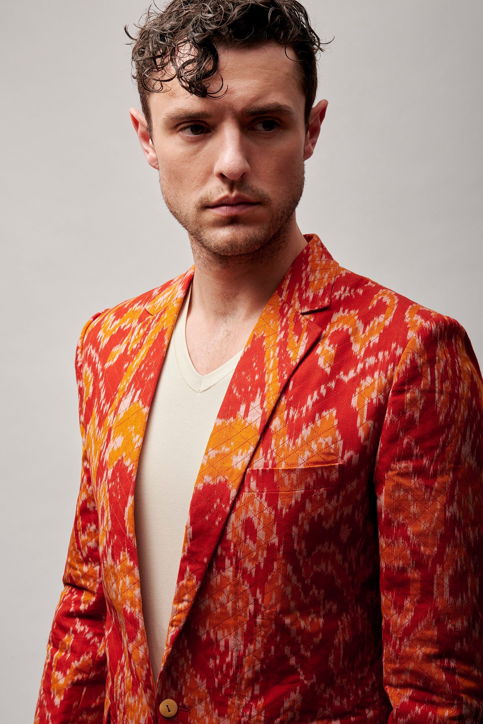 Model wearing a vermilion orange blazer. It is woven in shades of a sunset. 