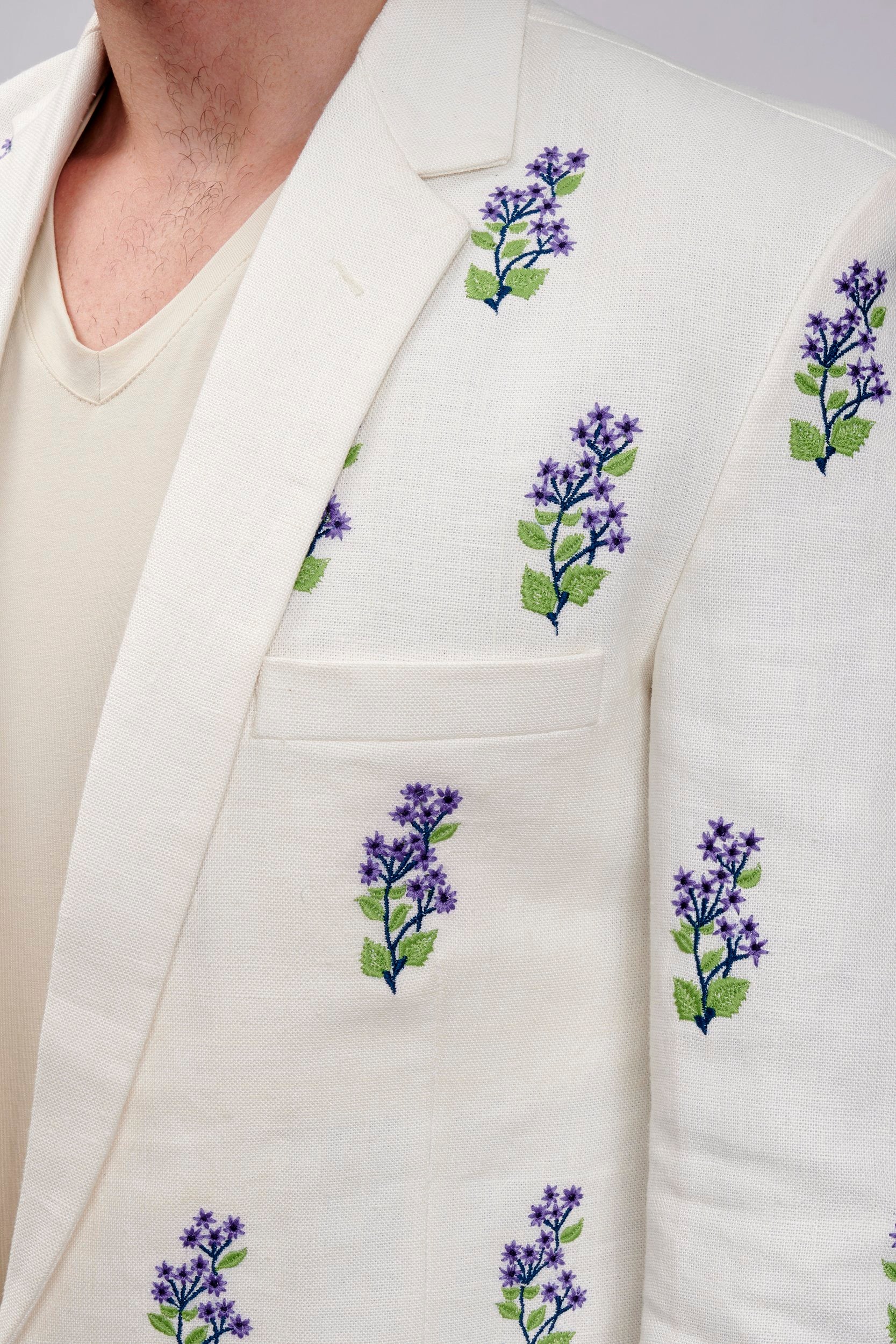 Closeup of model wearing an off-white embroidered blazer with lavender motifs made with Undyed yarn. 