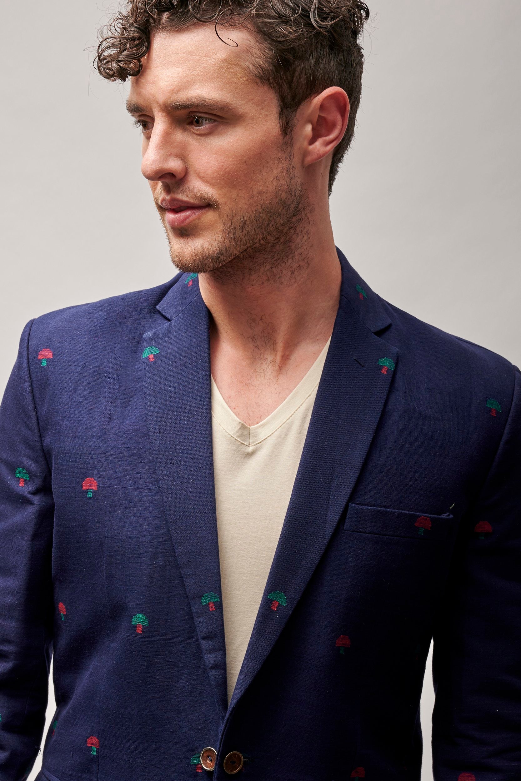 Model wearing a men's navy blue sports coat with red and green embroidered motifs. Made with khadhi fabric. 