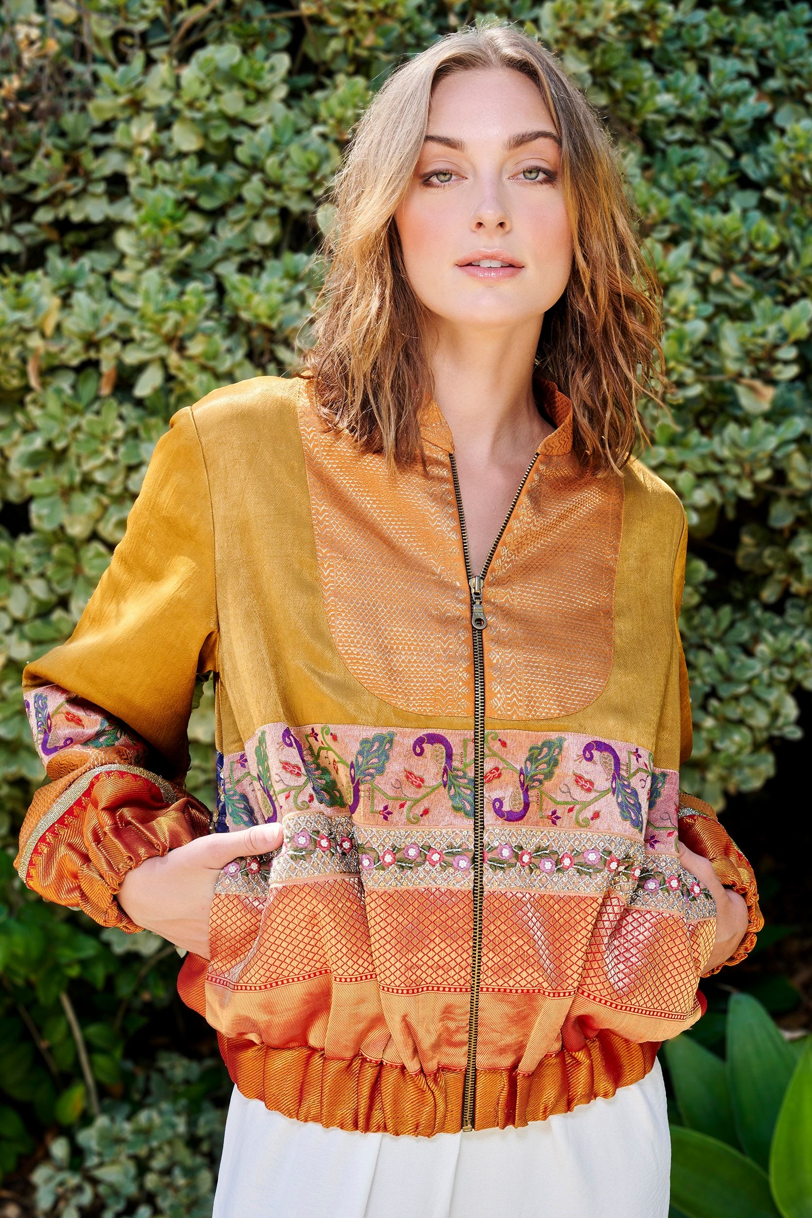 A woman wearing a gold and orange color handmade bomber jacket with gold embellishments on the back. 