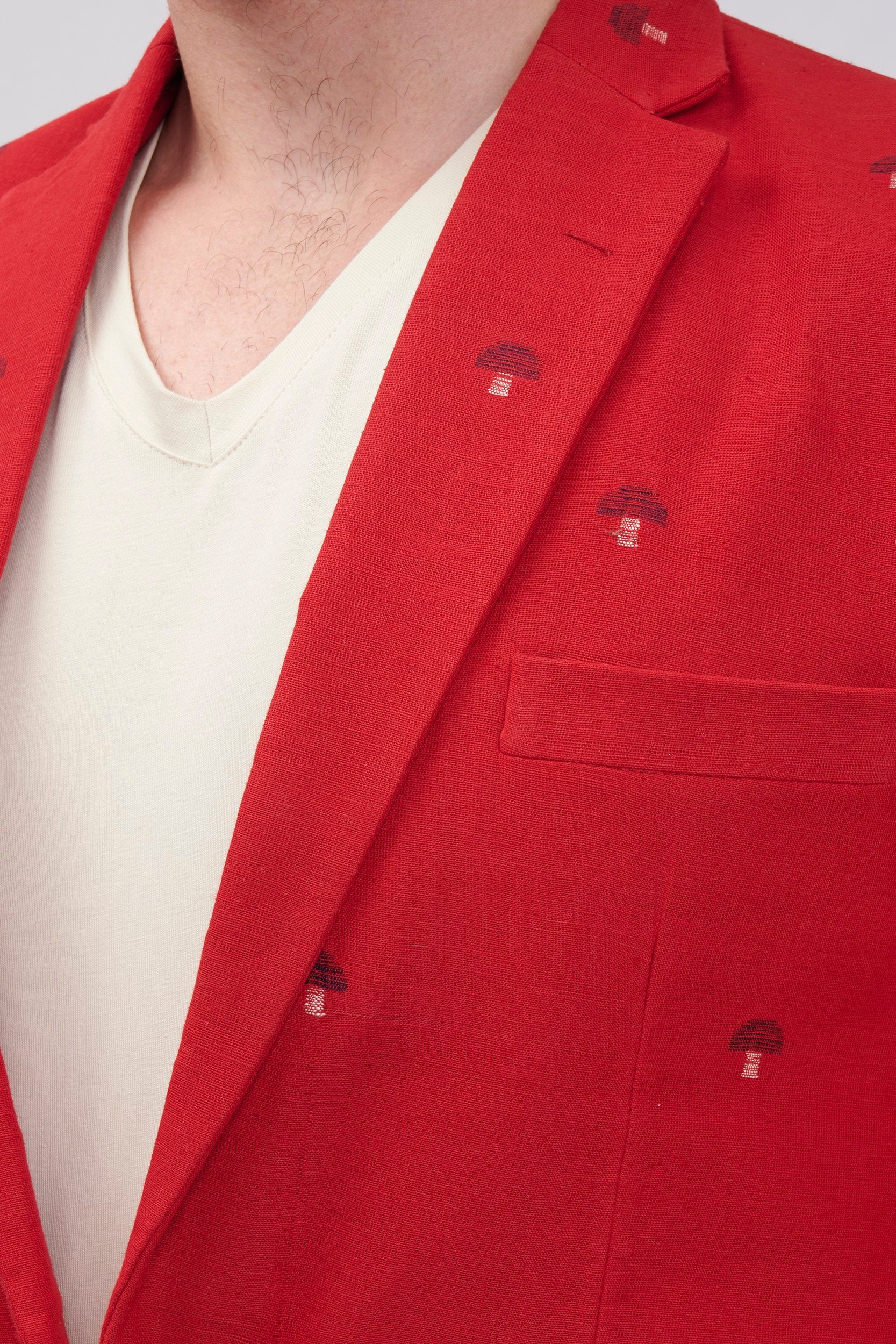 closeup of a red cotton blazer showcasing hand embroidered motifs on the surface.