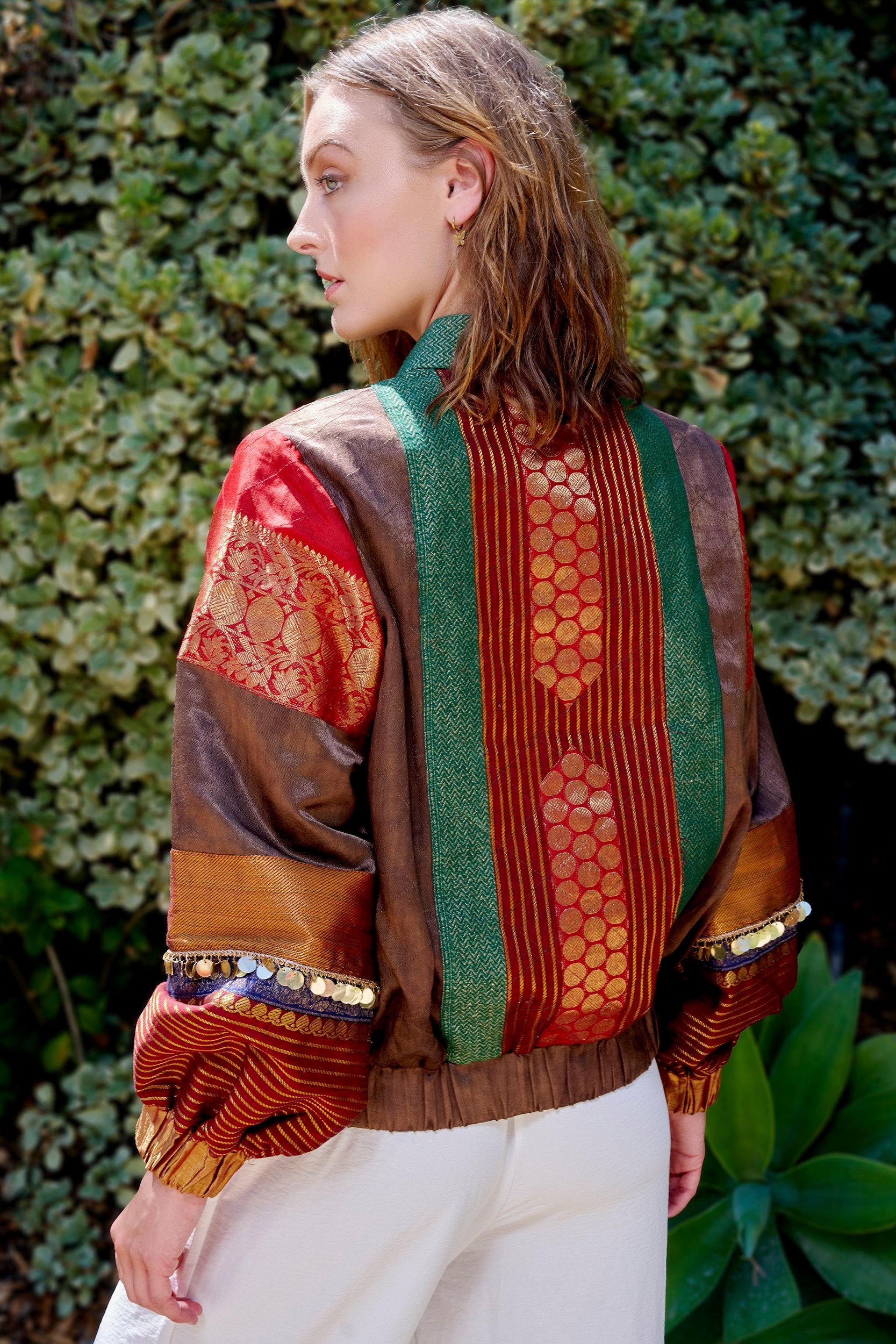 Model wearing a  bomber jacket in green and red color with gold embellishments on the sleeves.