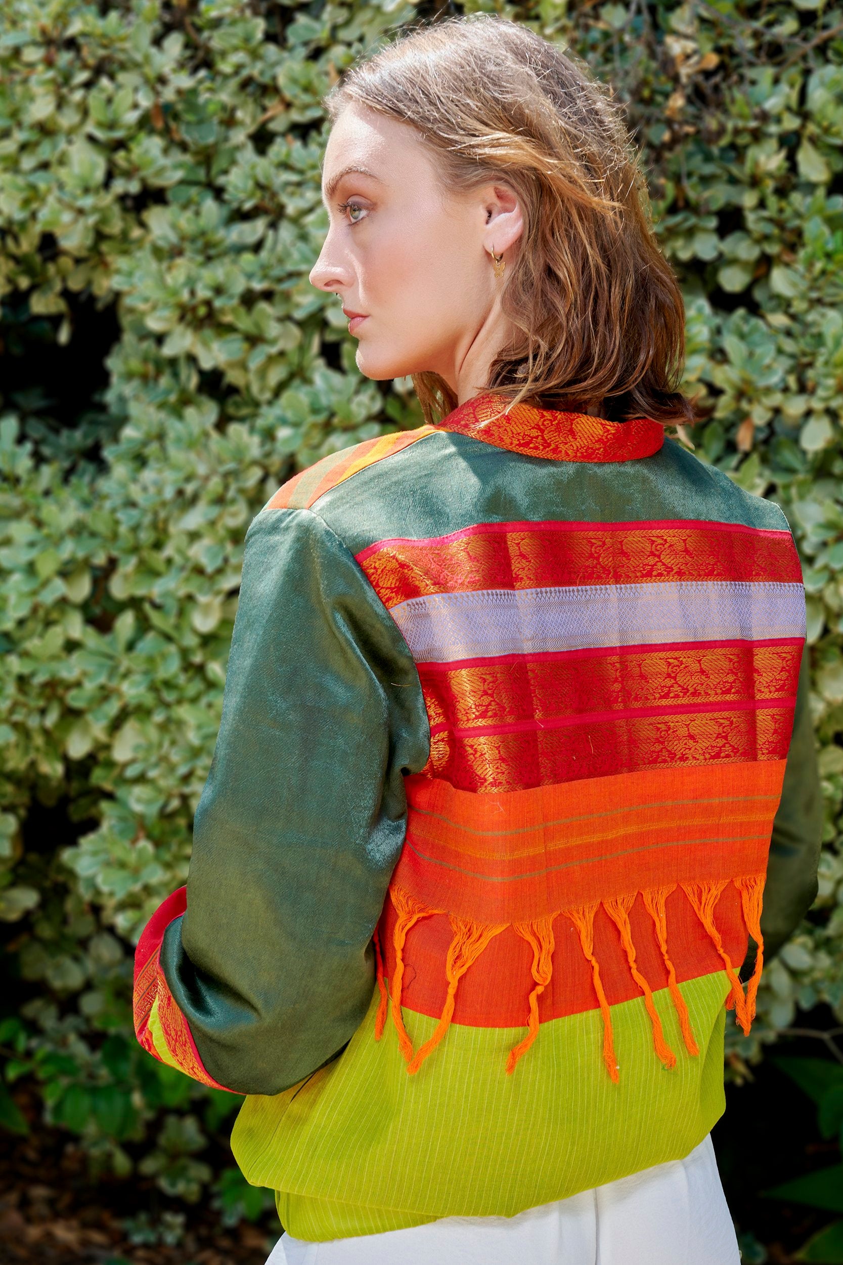 A woman wearing a sustainable Bomber Jacket with orange tassels on the back. It has a red zari border strips.