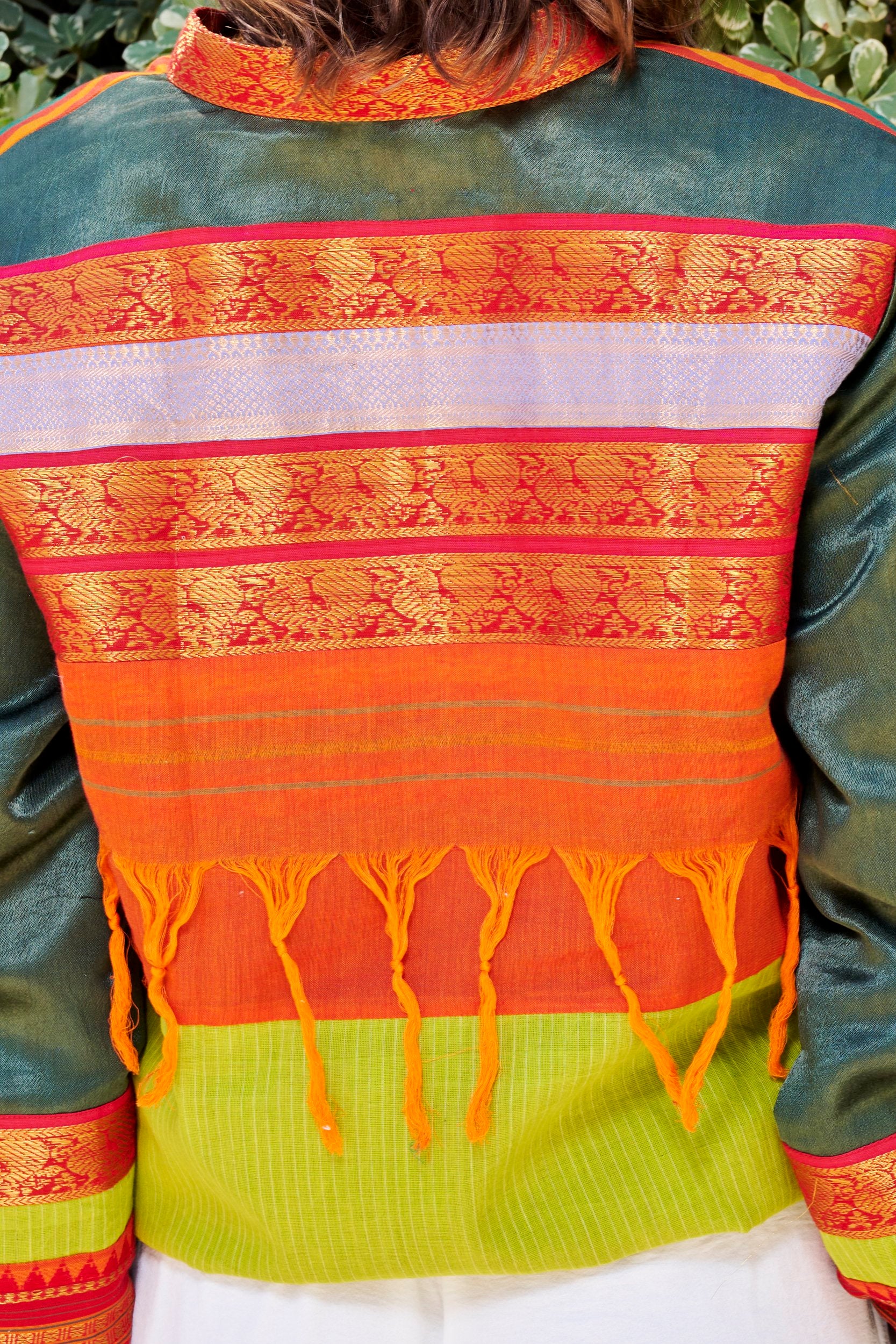 closeup of a bomber jacket back showcasing the intricate gold weave patterns and orange tassels.