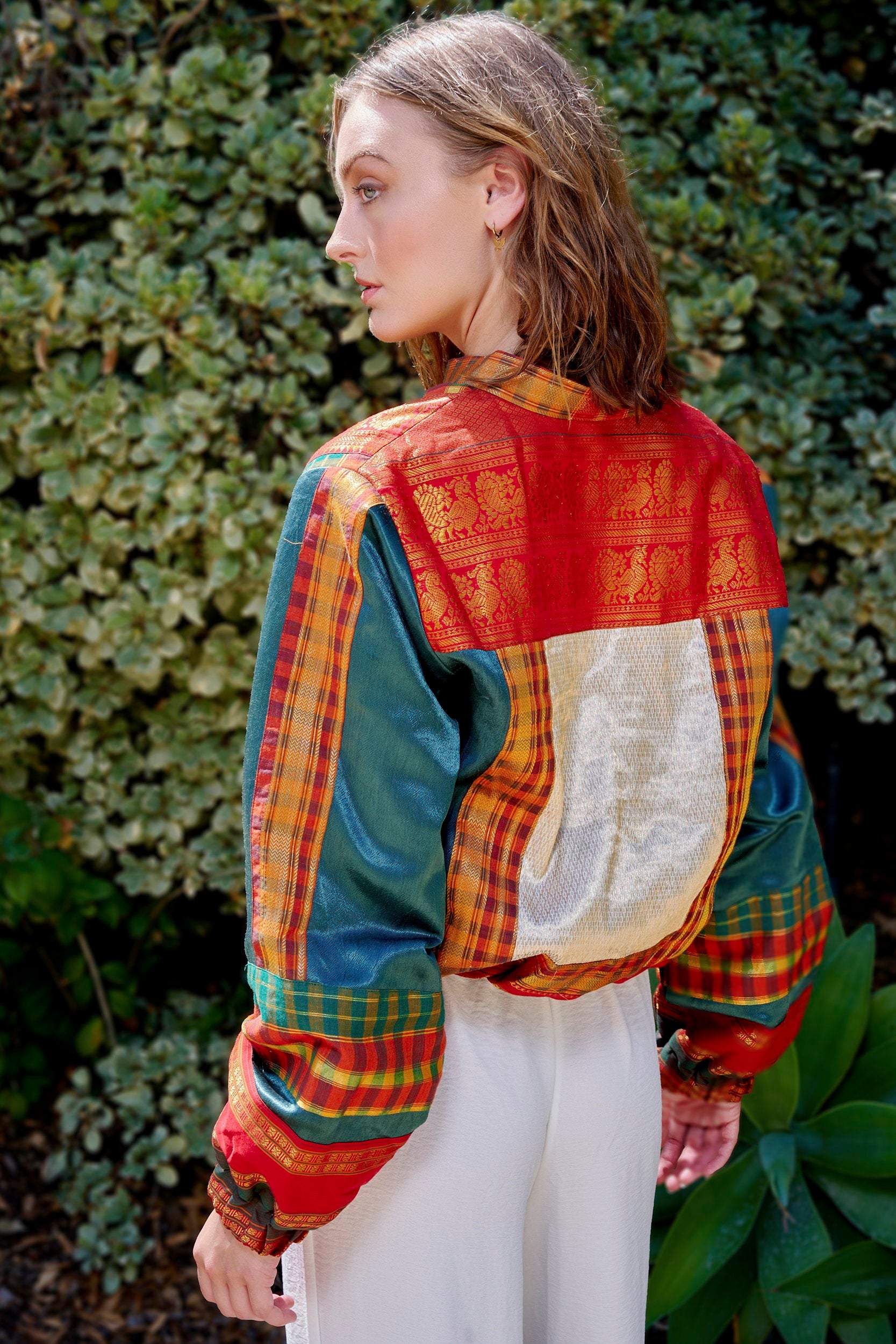 Model wearing a handmade green and red bomber jacket made from repurposed precious fabric remnants.