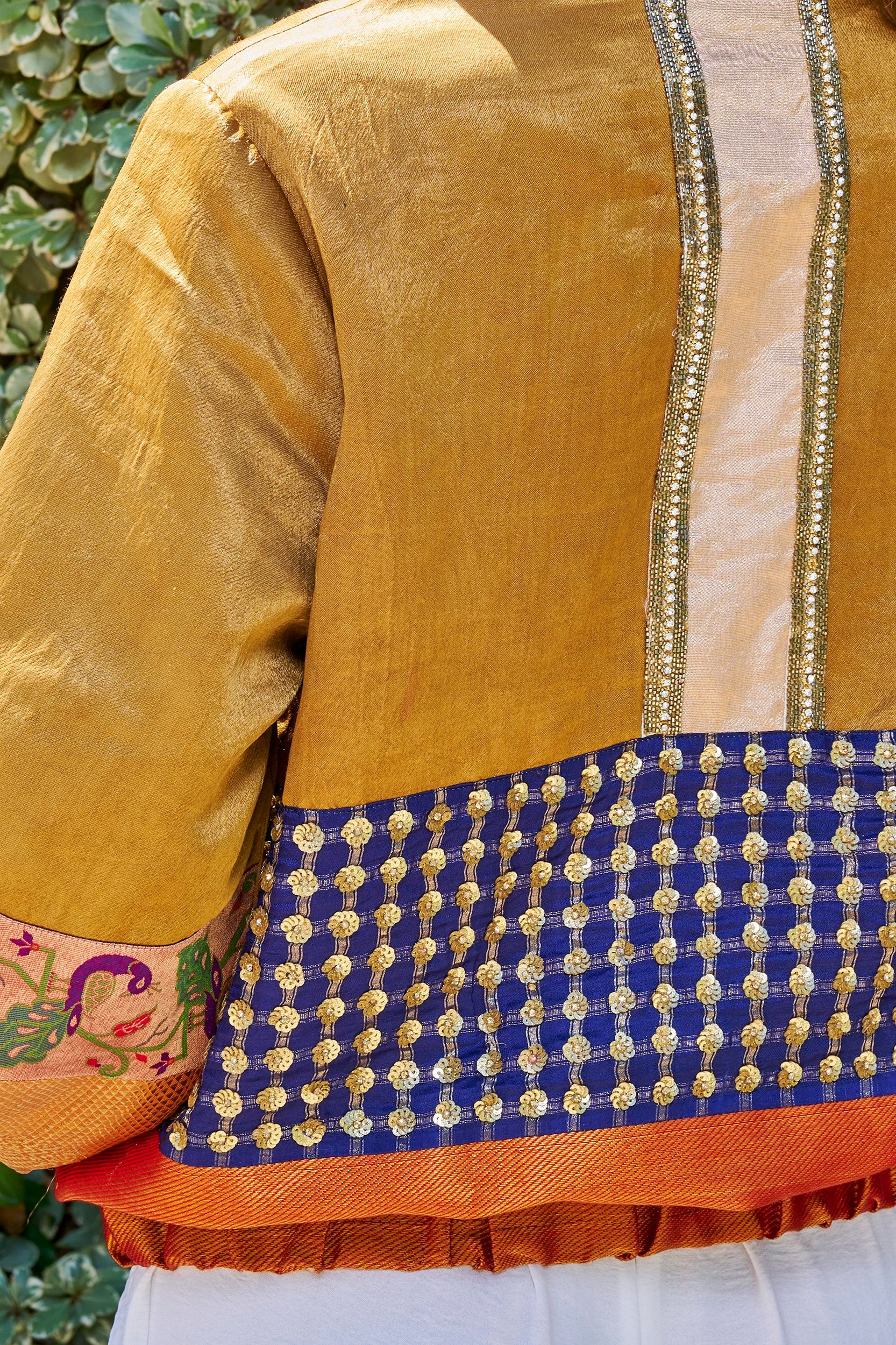 A woman wearing a gold and orange color handmade bomber jacket with gold embellishments on the back. 