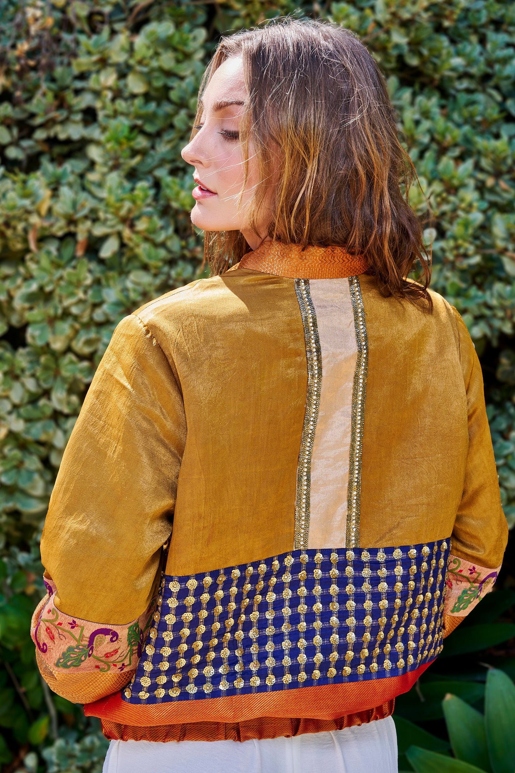 A woman wearing a gold and blue color handmade bomber jacket with gold embellishments on the back of the jacket.