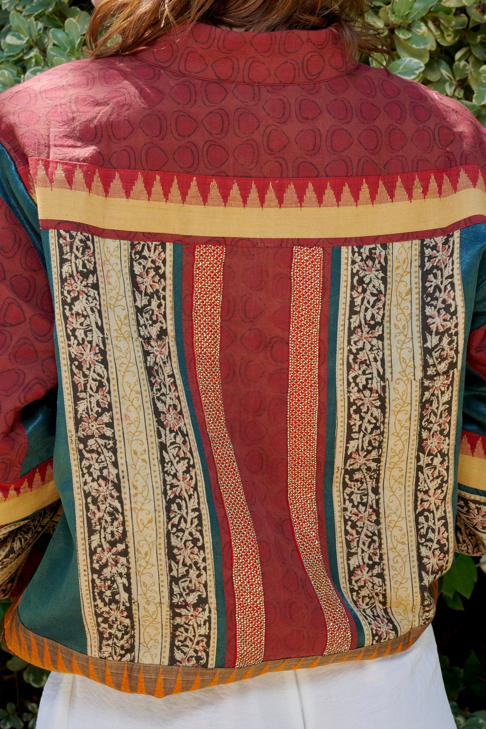 closeup shot of bomber jacket back showcasing hand block print pattern in wine red and yellow floral strips. 