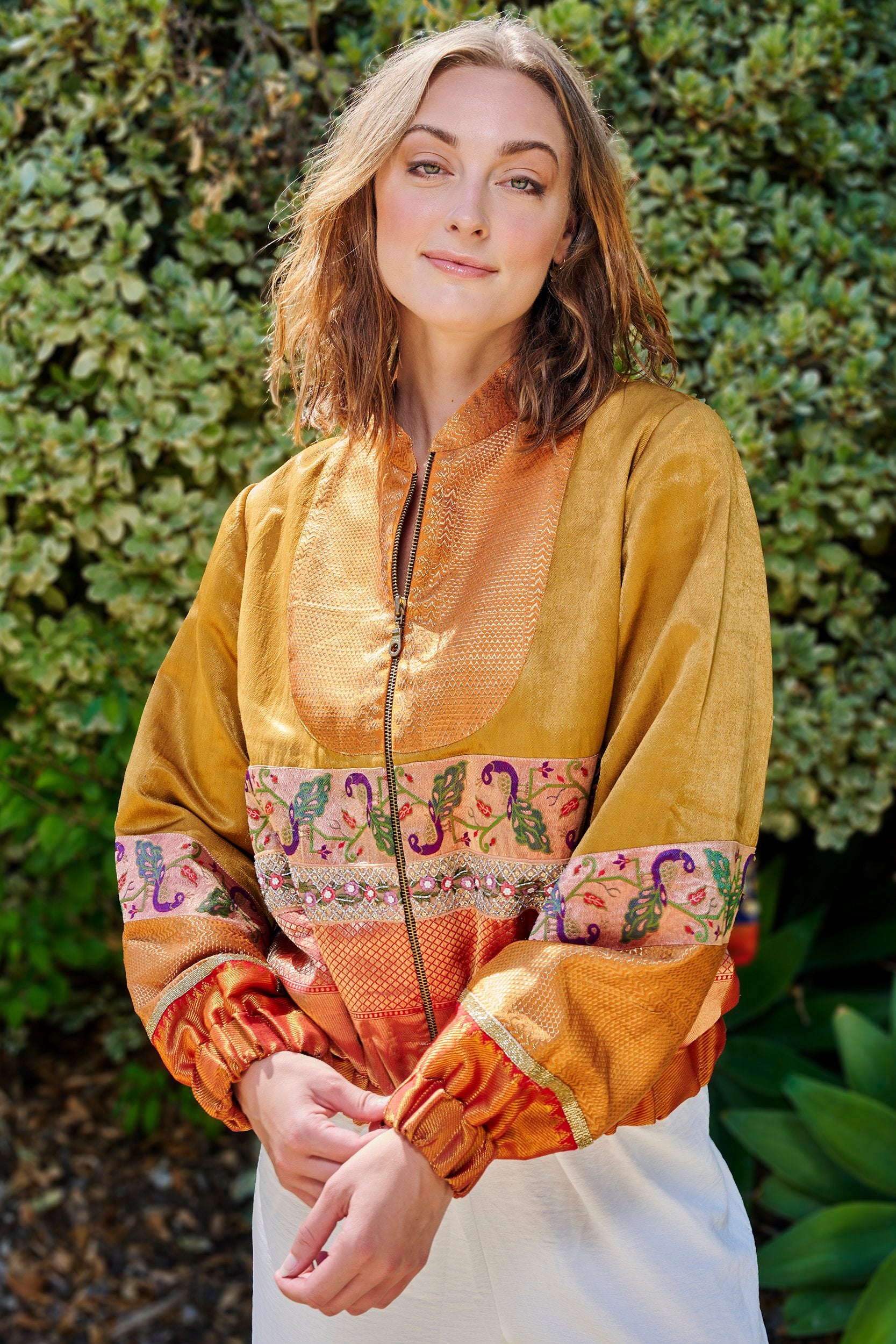 A woman wearing a gold and orange color handmade bomber jacket. Handmade from repurposed precious fabric remnants.