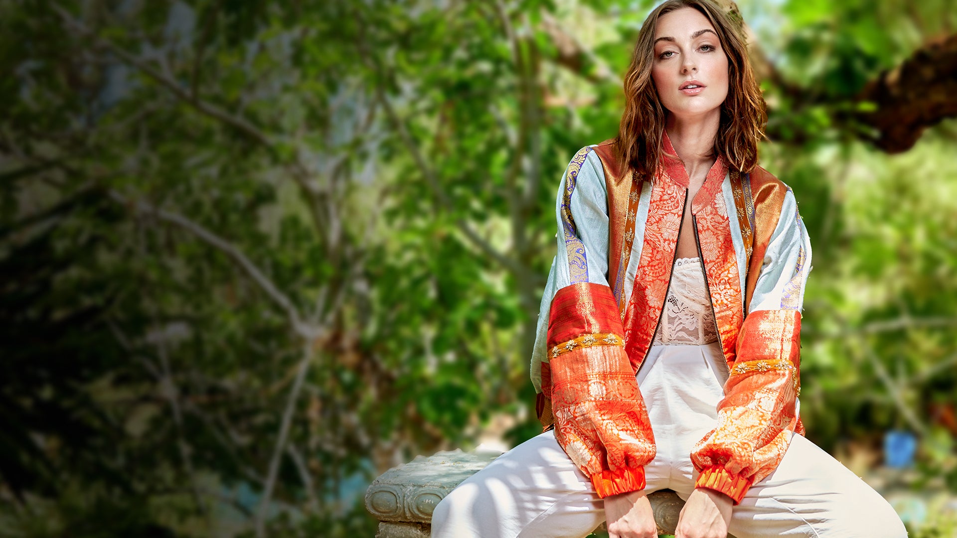 A model wearing a sustainable bomber jacket in orange and ivory colors.